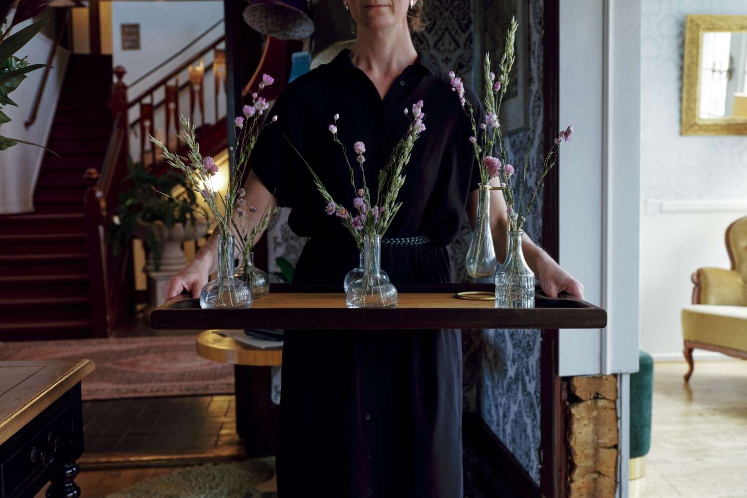 Person bär bricka med blommor i hotellmiljö på Grenna Hotell