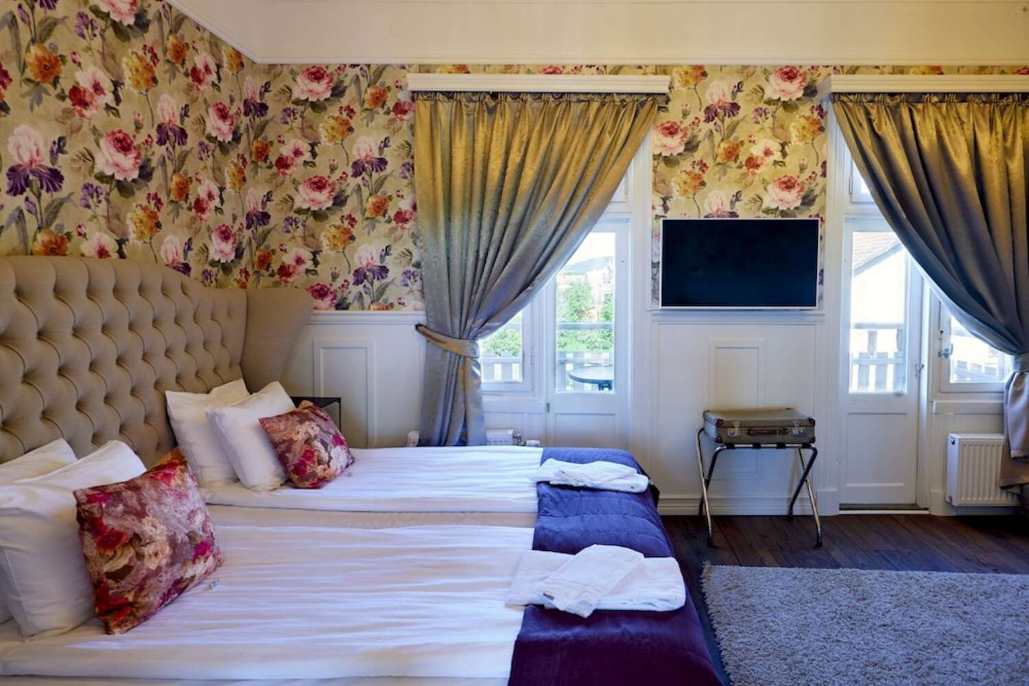 Hotellrum med blommig tapet, två sängar och tv på Grenna Hotell