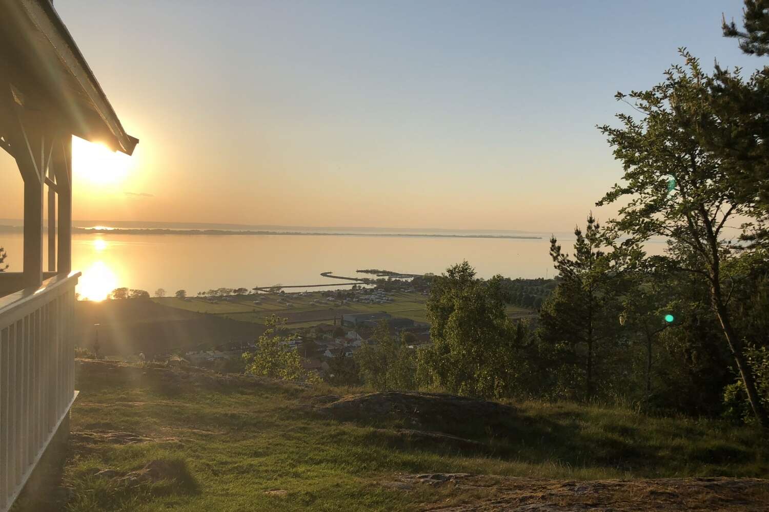 Utsikt över Vättern i kvällssol från höjd med träd och hus