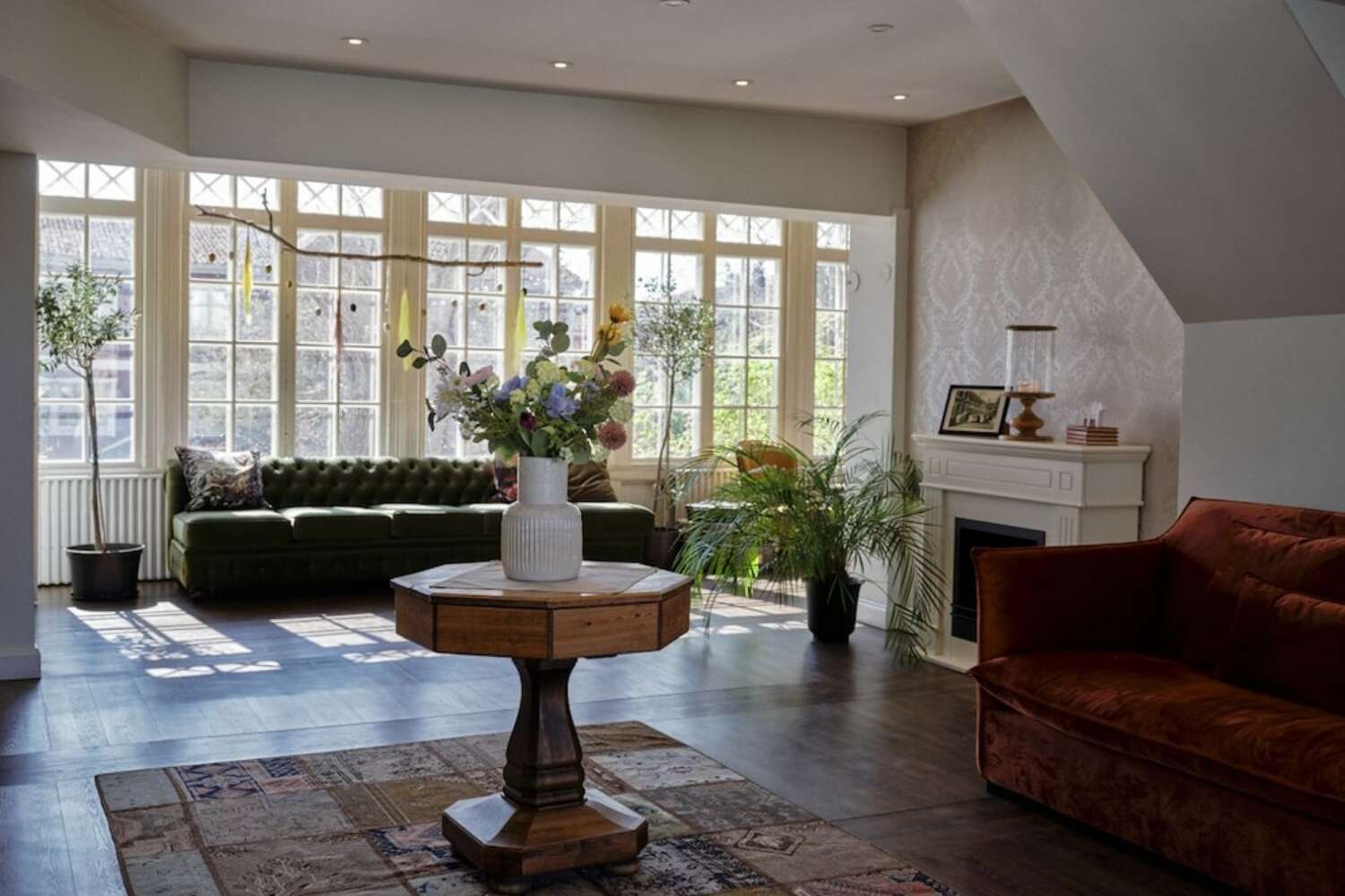Lounge med soffor, blommor och stora fönster på Grenna Hotell