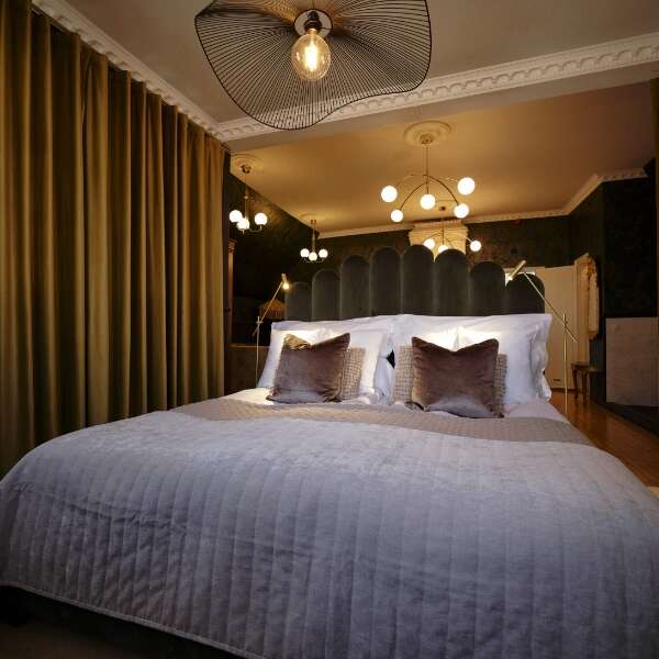 Bäddad dubbelsäng med dekorativa lampor och mörka gardiner i Greta Garbo Sviten på Grenna Hotell