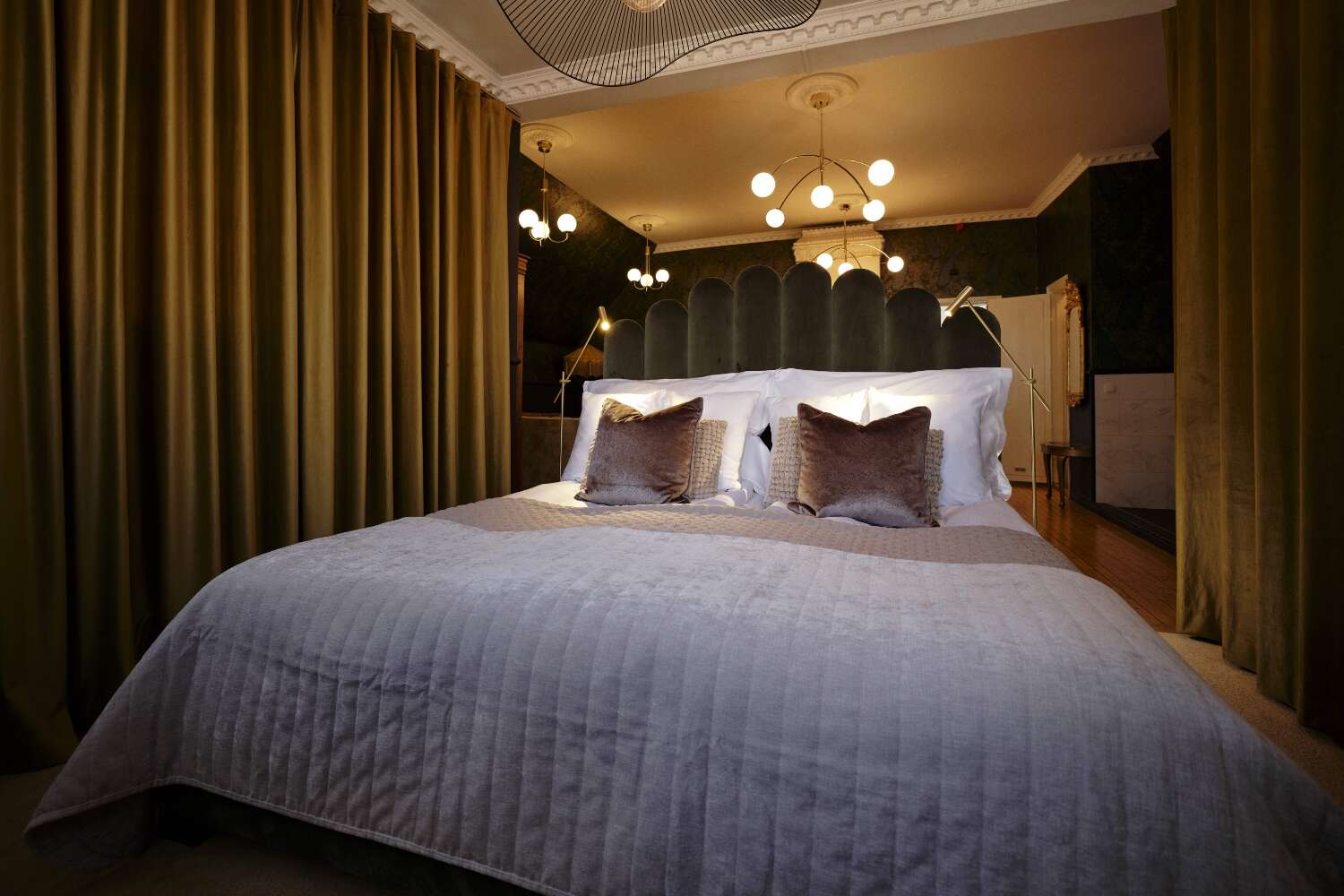 Dubbelsäng med sammetsgavel, draperier och taklampor i varm belysning